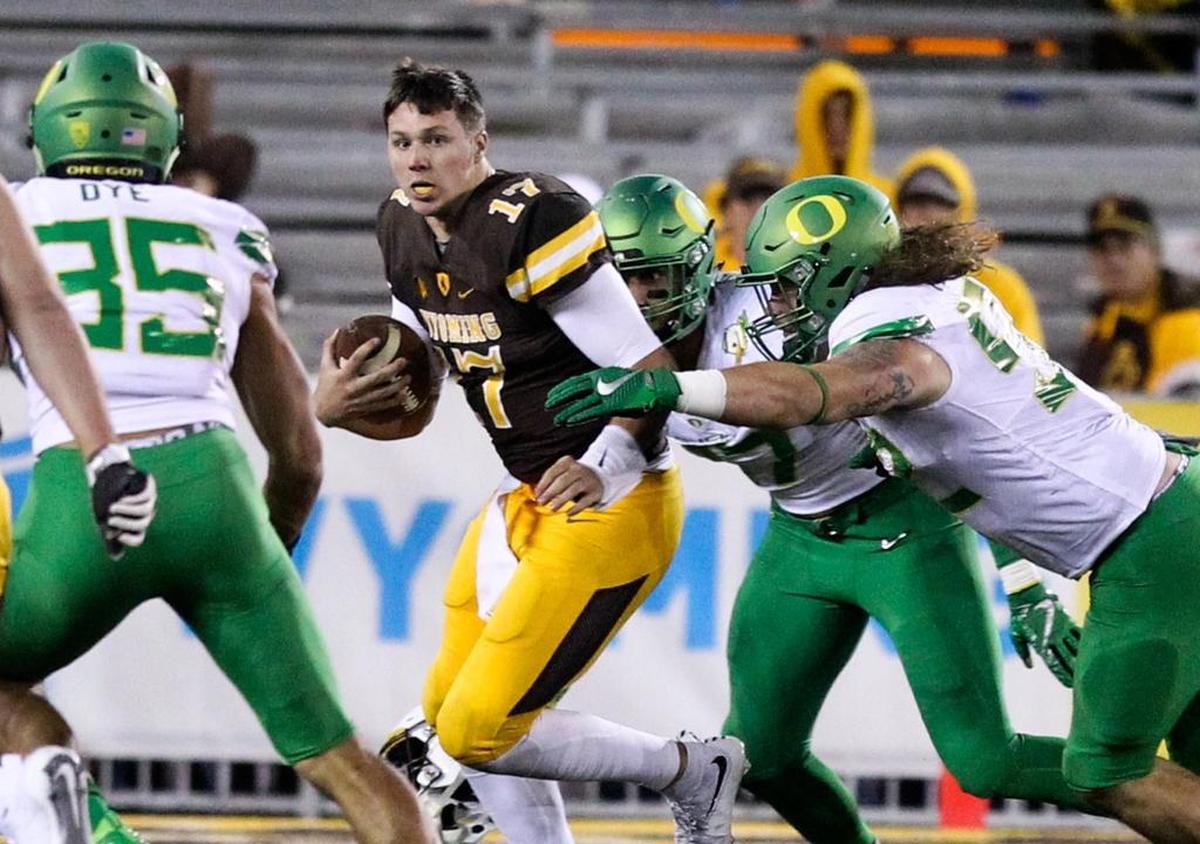 Wyoming quarterback Josh Allen runs past Oregon defenders after losing his helmet during the second half of an NCAA college football game in Laramie, Wyo., Sat., Sept. 16, 2017.