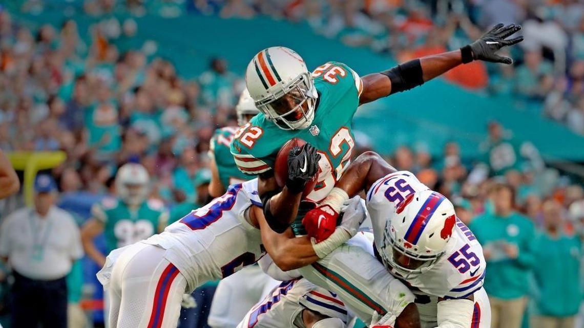 The Dolphins’ Kenyan Drake (32) is tackled by the Bills’ Micah Hyde (23) and Jerry Hughes (55) in the first quarter at Hard Rock Stadium in Miami Gardens Sunday, Dec. 31, 2017.
