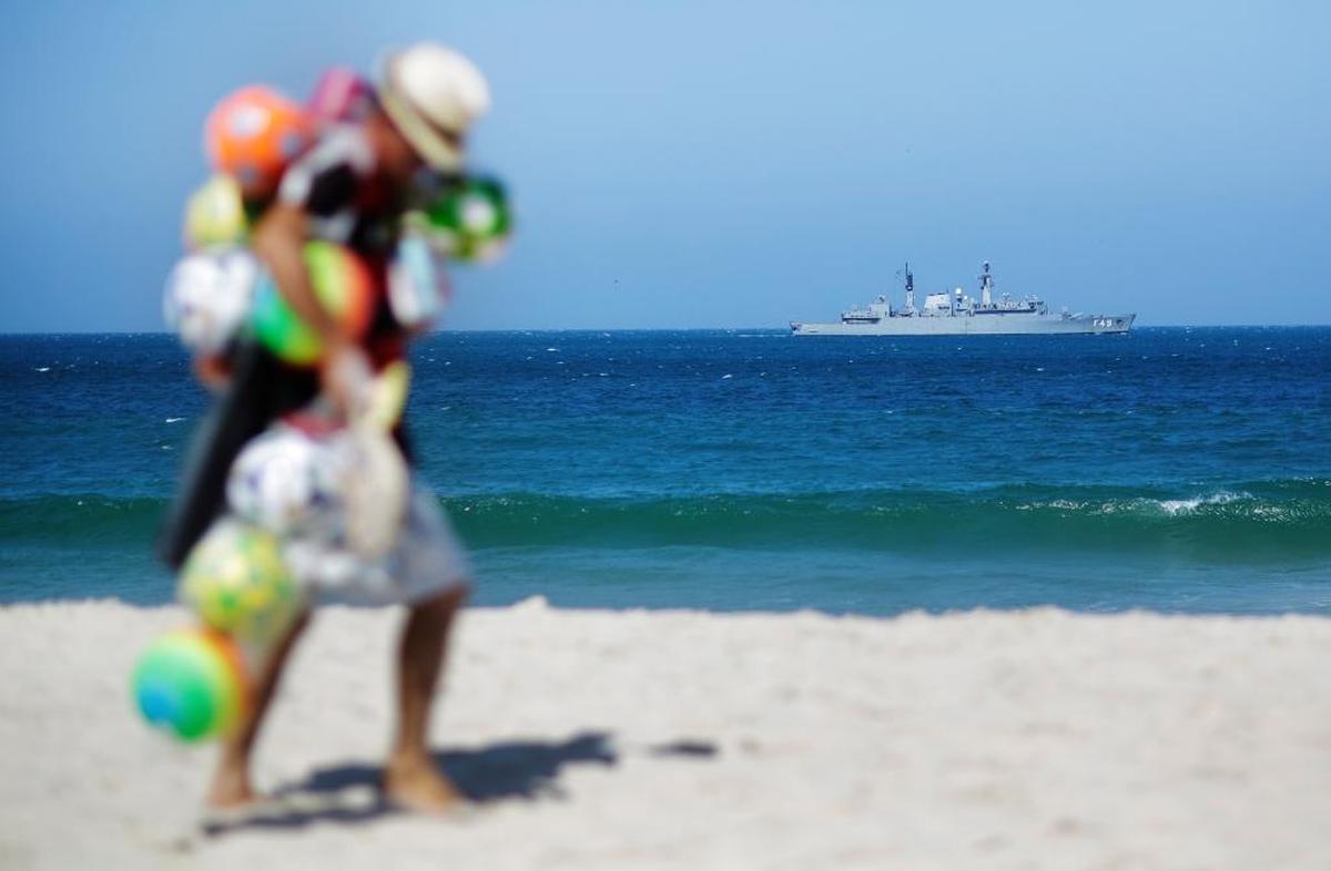A vendor selling soccer balls at Copacabana Beach walks by as a military ship patrols the waters ahead of the Summer Olympics in Rio de Janeiro, Brazil. You can buy one of the soccer balls for $8.