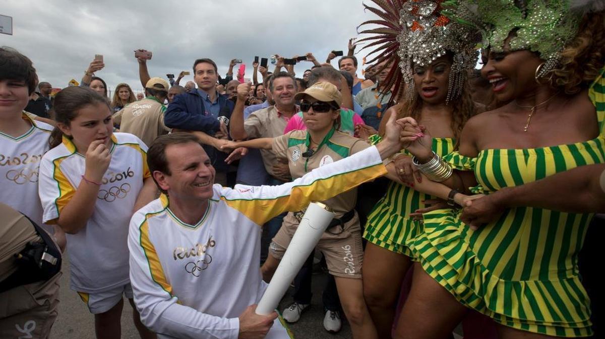 Rio de Janeiro’s Eduardo Paes, center, holds the Olympic torch while members of the Mangueira samba school dance Wednesday after the arrival of the flame, which will head to the Maracana stadium for Friday’s Opening Ceremonies.