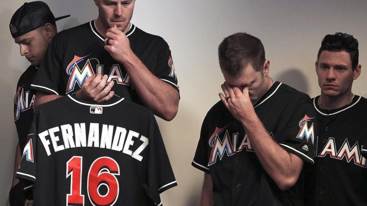 Miami Marlins closer, A.J. Ramos, left, bows his head as Mike Dunn, pitcher, second from the left, holds the jersey belonging to Jose Fernandez while standing with teammates during the team's news conference, Sunday, September 25, 2016